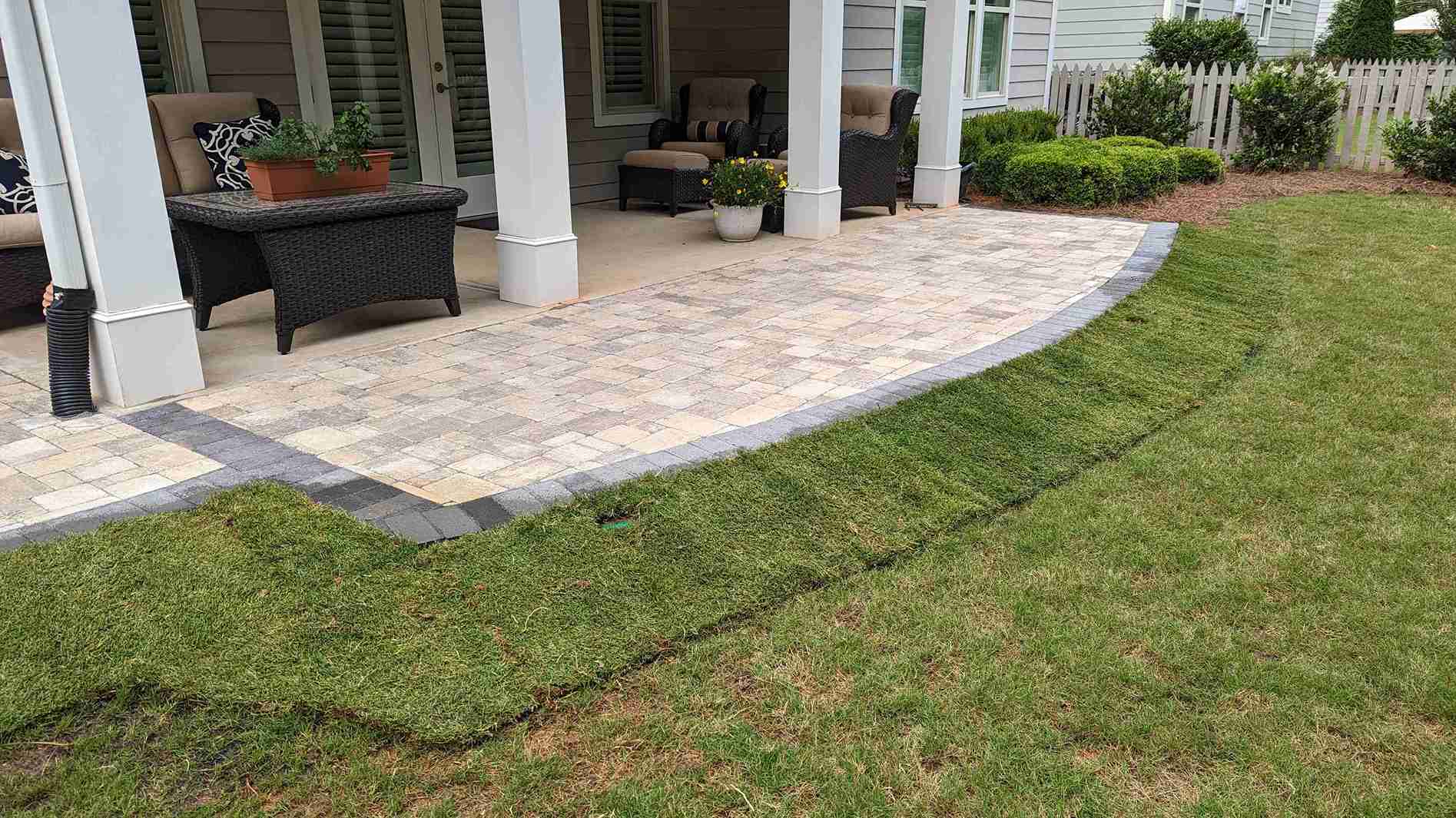 Paver patio extending a covered porch, edged with a charcoal border course and fresh sod