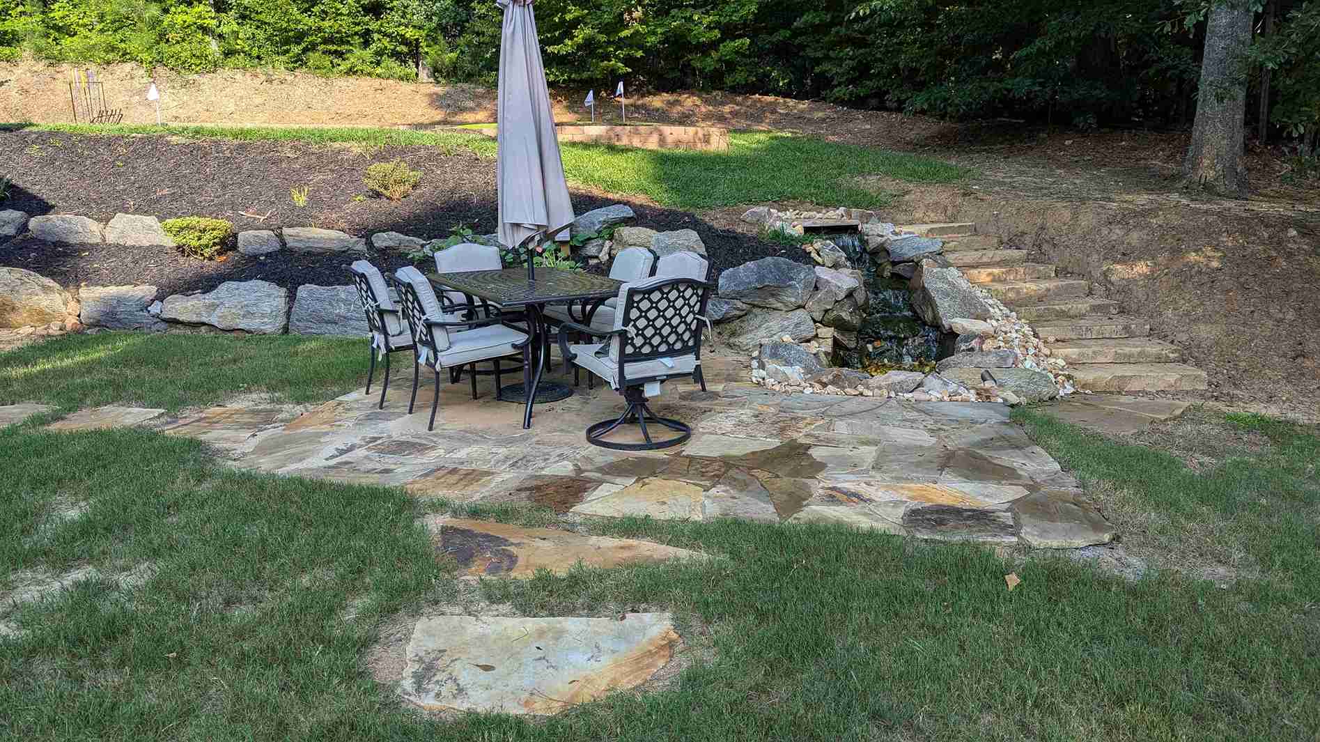 Flagstone dining patio with a stacked stone wall, a rock waterfall and natural stone steps