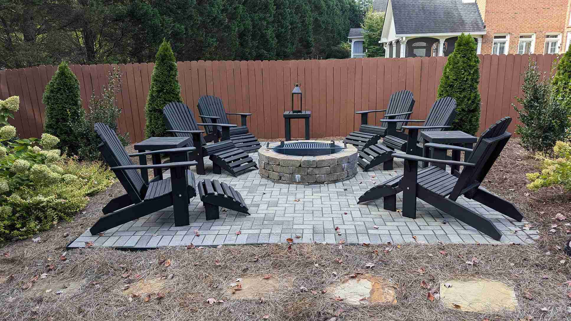 Paver fire pit patio with a stone fire ring, black Adirondack chairs and hydrangea plantings