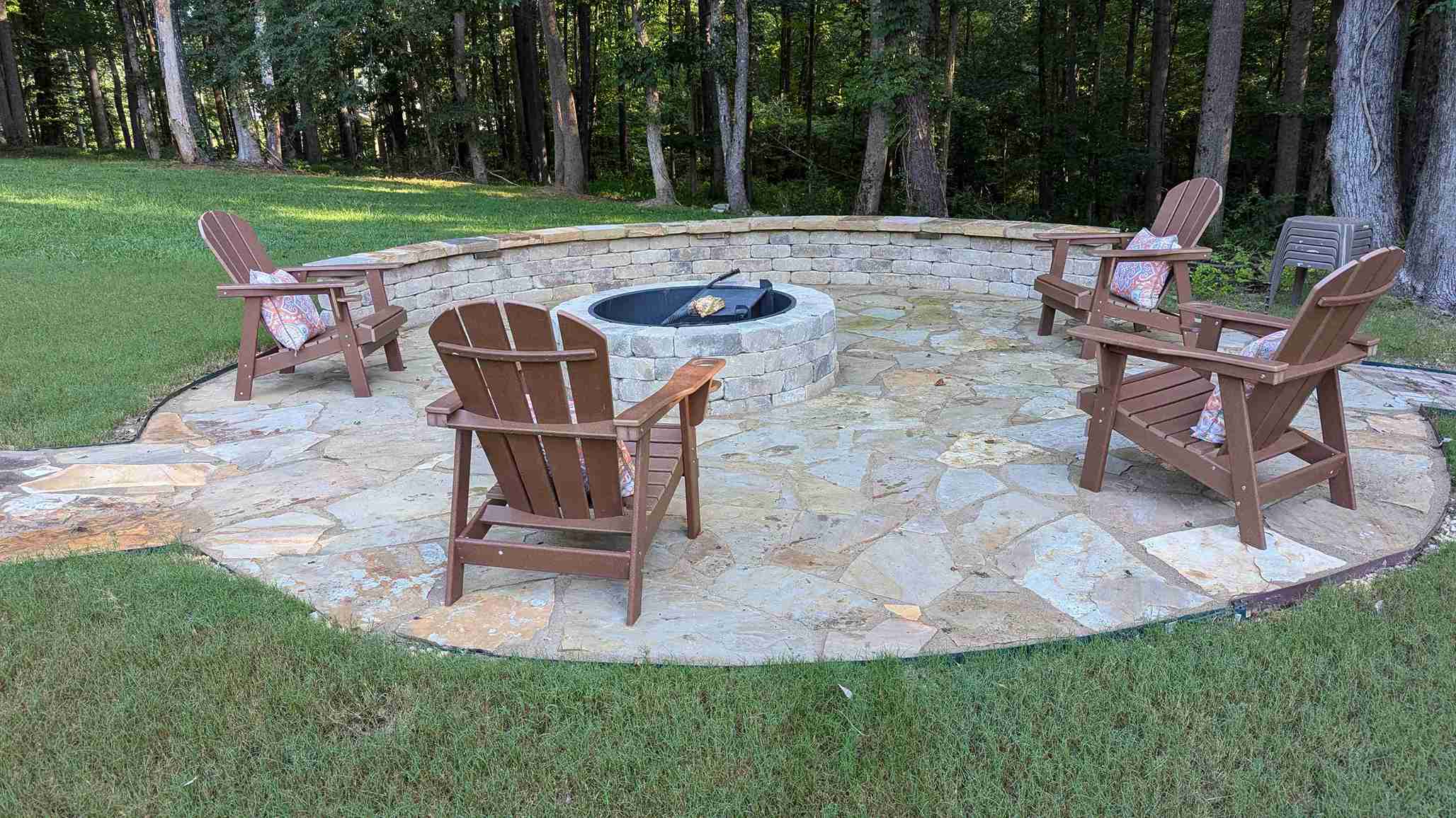 Flagstone fire pit patio ringed by a curved stone seating wall and Adirondack chairs at the edge of the woods