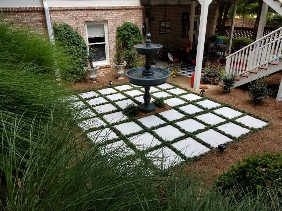 Courtyard fountain set in a white paver grid with planted turf joints and ornamental grasses